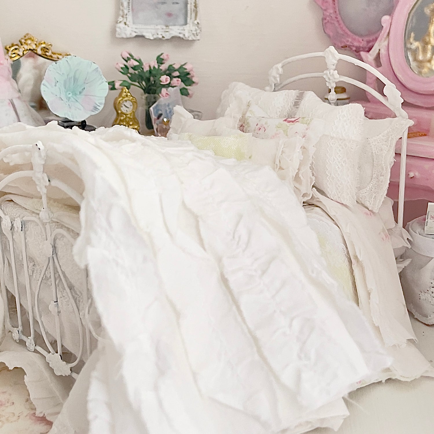 Delicate white lace dollhouse bedding set on a white bed with decorative items in the background. Chantallena